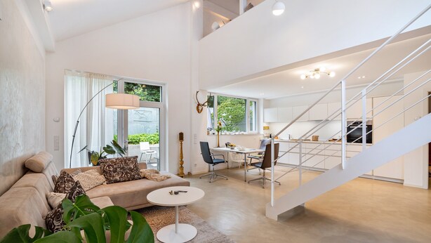 Un vaste espace de vie comprenant un canapé, une table basse et une table à manger avec des chaises. Un escalier mène à l’étage supérieur.