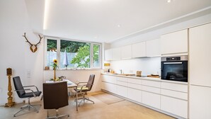 Une cuisine moderne avec des armoires blanches, un four encastré et un coin repas comprenant deux chaises et une table.