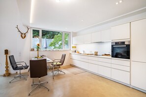 Une cuisine moderne avec des armoires blanches, un four encastré et un coin repas comprenant deux chaises et une table.