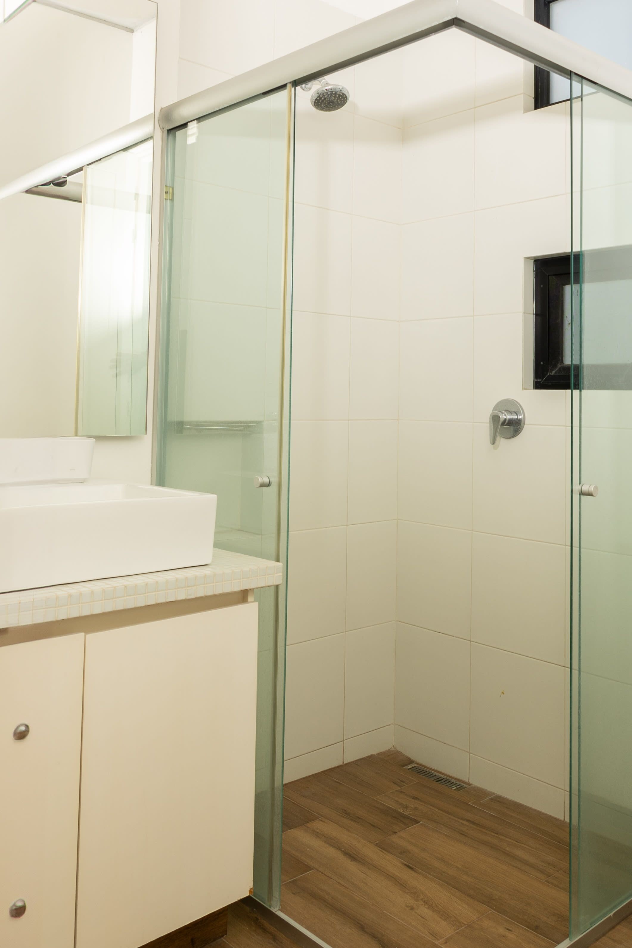 A modern bathroom with a glass-enclosed shower, a white sink, and a wooden floor.