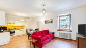 A compact living space with a kitchenette, a red sofa, a dining table, and a large window. - La Madonnina Apartment for 2 in Tenno (Tenno)
