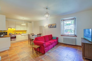Un espacio habitable compacto con kitchenette, un sofá rojo, una mesa de comedor y un televisor.