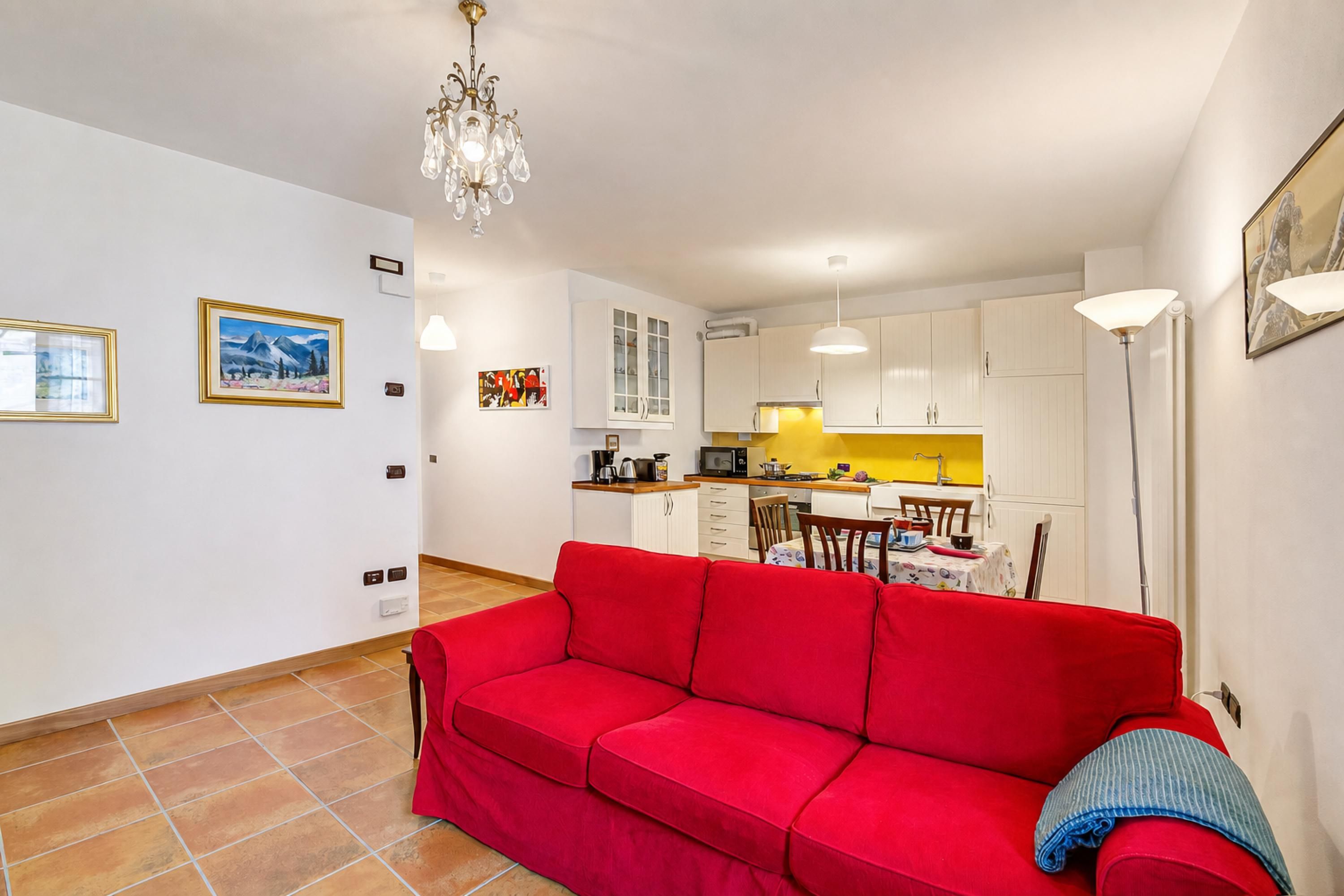 Un espacio habitable compacto con un sofá rojo, una zona de comedor, una cocina con armarios blancos y una araña.