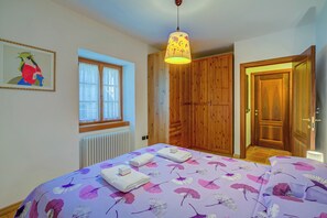 Un dormitorio con cama, ventana, radiador, armarios de madera y una puerta.