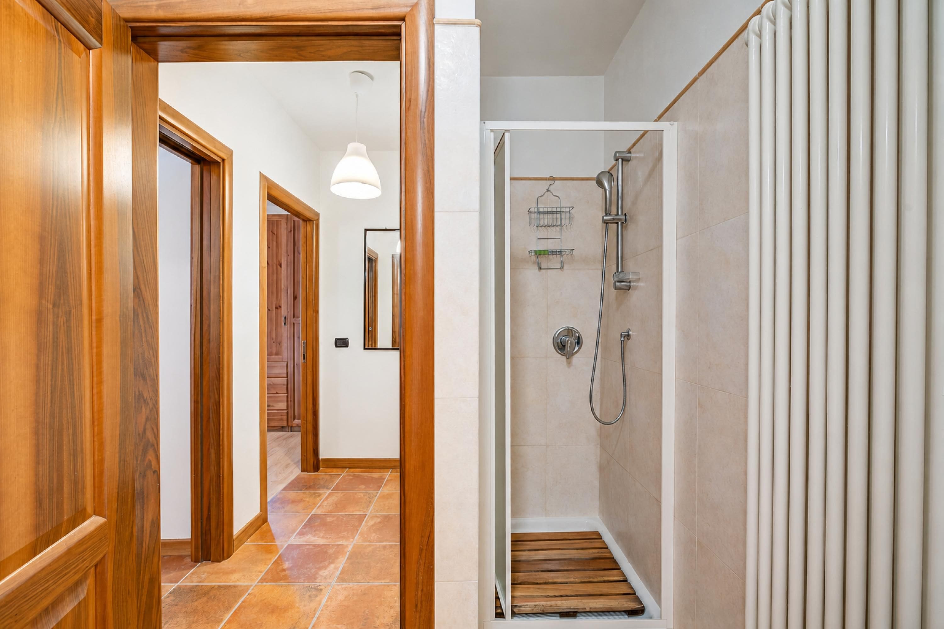 A hallway with wooden doors, a shower area with a white tiled wall, and a hanging light fixture.