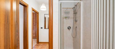 A hallway with wooden doors, a shower area with a white tiled wall, and a hanging light fixture.