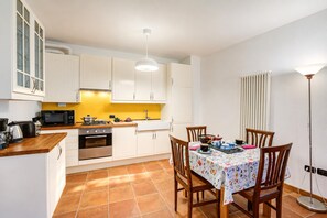 A compact kitchen with white cabinets, a microwave, a stove, and a dining table with chairs. - La Madonnina Apartment for 2 in Tenno (Tenno)