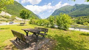 A picnic area with benches and a table, surrounded by lush greenery and mountains in the background. - La Madonnina Apartment for 2 in Tenno (Tenno)