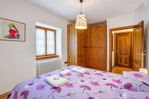 A bedroom with a bed, a window, a wooden wardrobe, and a door. - La Madonnina Apartment for 2 in Tenno (Tenno)