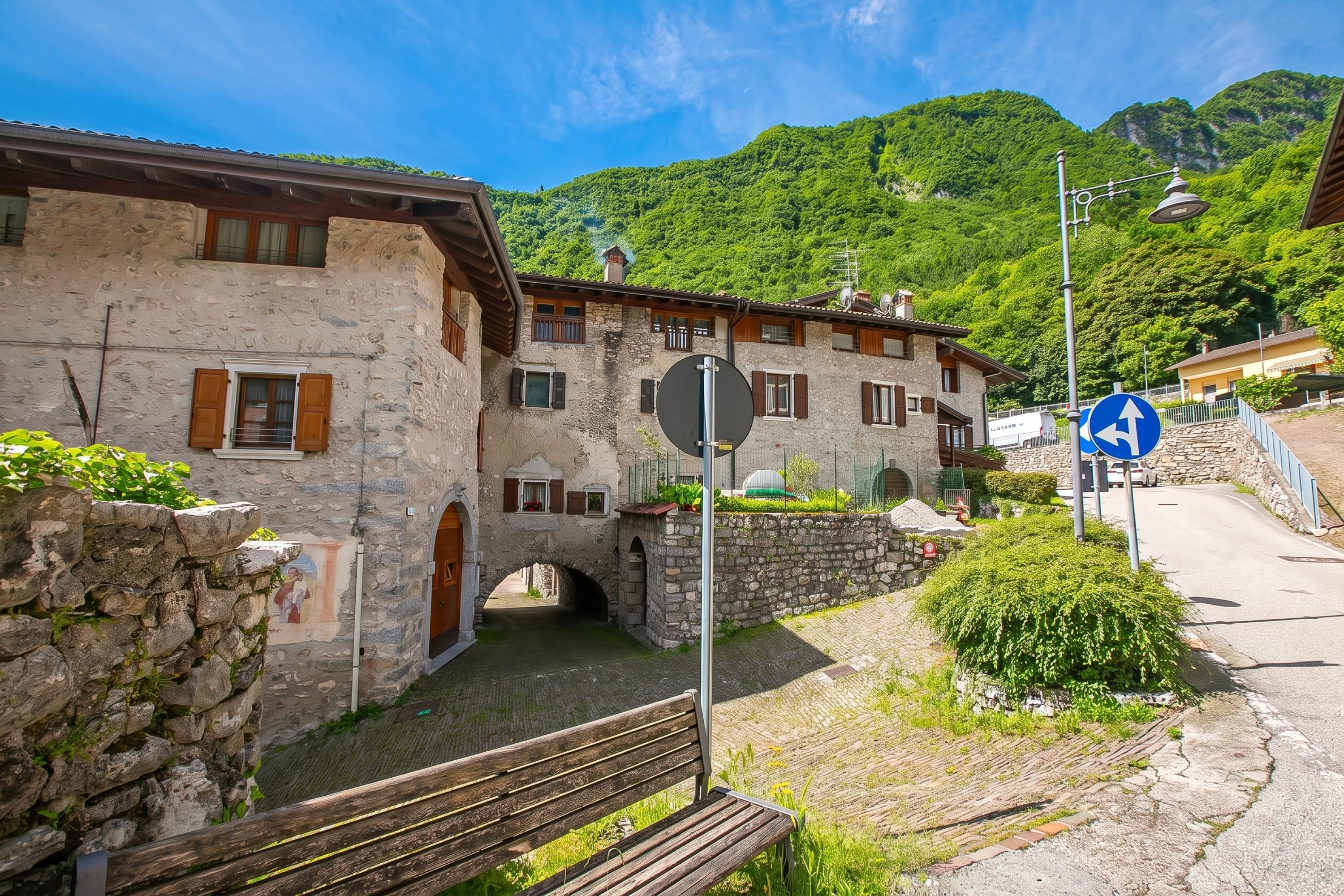 Ein Steinhaus mit rustikalem Aussehen, eine kleine Brücke und ein Wegweiser, der eine Abzweigung anzeigt.