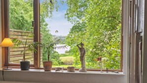 A room with a large window overlooking a lush garden and a lake.