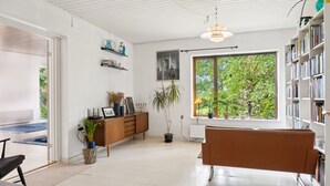 A spacious living room with a large window, a bookshelf, a brown sofa, and a wooden cabinet.