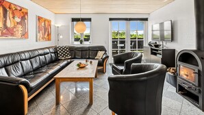 A modern living room with a black leather sofa, a wooden coffee table, and black armchairs. There is a fireplace and a TV mounted on the wall. - "Birette" - 1.2km from the sea by Interhome (Ulfborg)