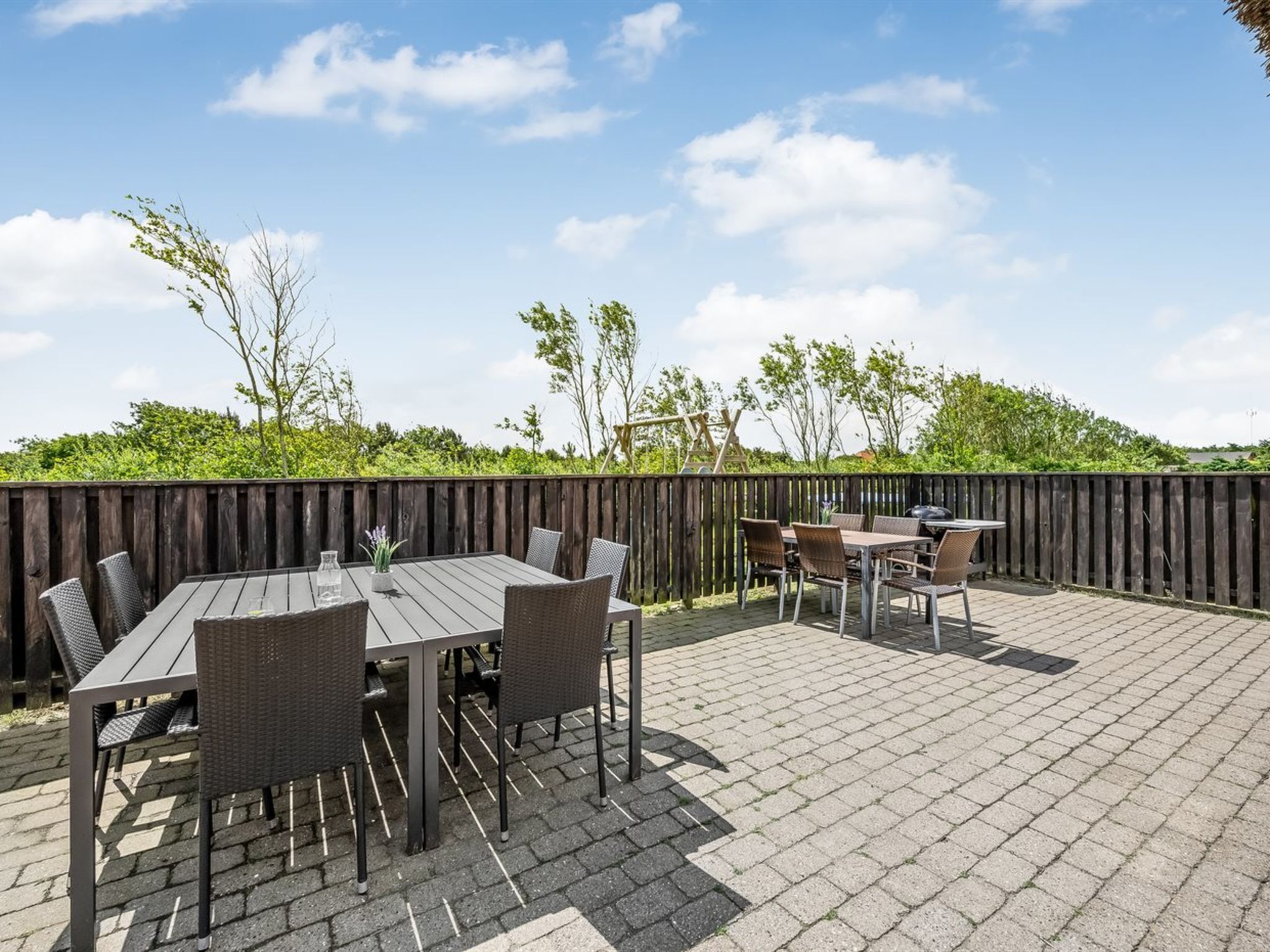 An outdoor patio with a wooden table and chairs, a grill, and a wooden fence.