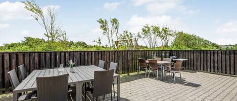 An outdoor patio with a wooden table and chairs, a grill, and a wooden fence.