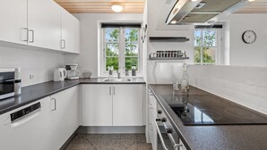 A modern kitchen with white cabinets, a black countertop, a built-in oven, and a window with a view of greenery. - "Birette" - 1.2km from the sea by Interhome (Ulfborg)
