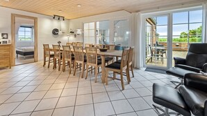 A spacious dining area with a wooden table and chairs, a kitchen area with a stove and cabinets, and a large sliding glass door leading to an outdoor patio with a brick wall and greenery.