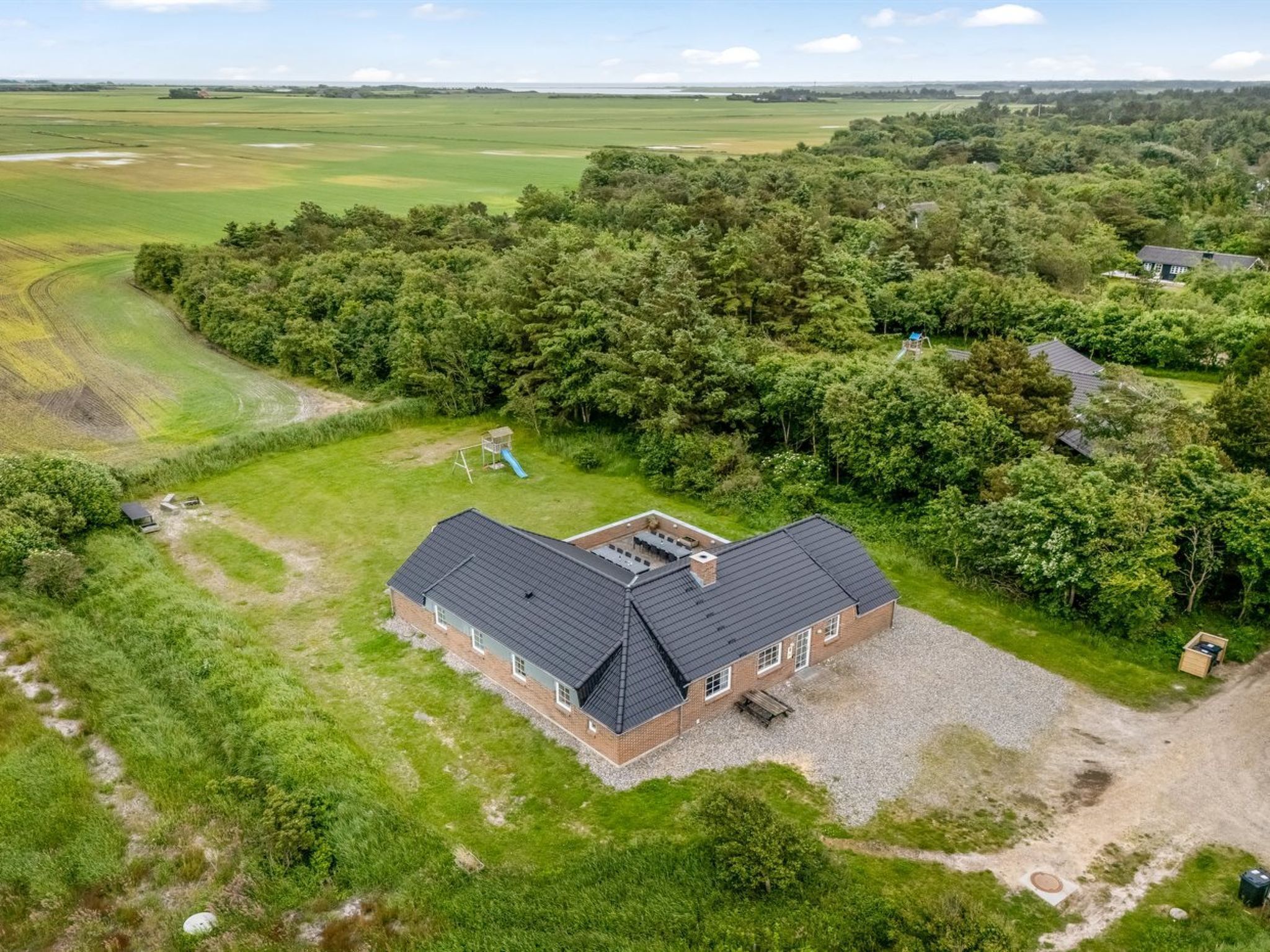 A large house with a spacious backyard, surrounded by lush greenery and fields.