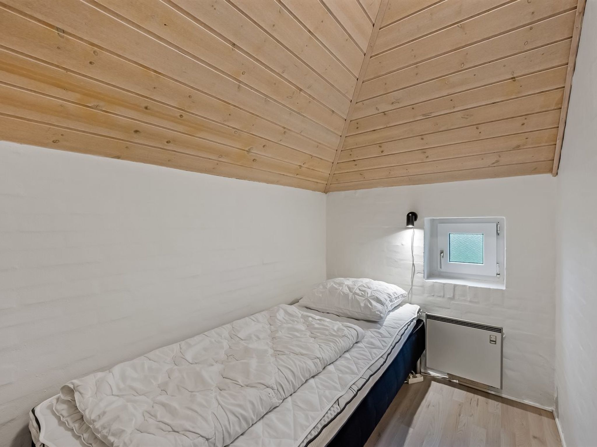 A small, single-bed room with a sloped ceiling, a window with a view, and a built-in heater.