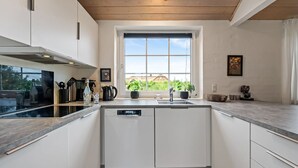 A modern kitchen with white cabinets, a built-in dishwasher, a window with a view, and a wooden ceiling.