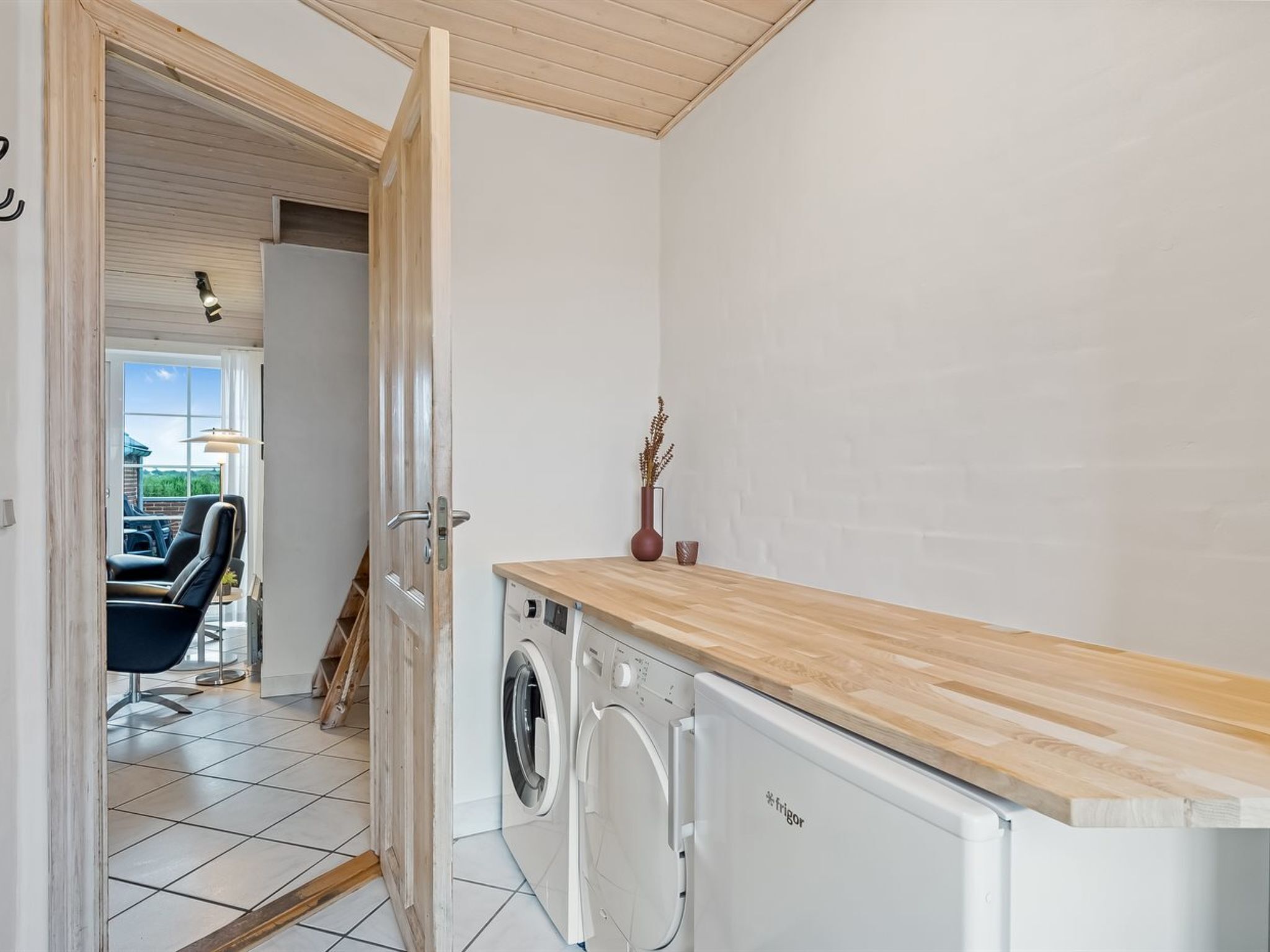 Un lavadero con lavadora y secadora, una encimera de madera y una puerta que da a una zona de estar con vistas al exterior.