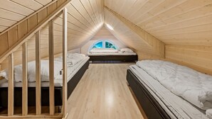 A small attic bedroom with wooden walls, a sloped ceiling, and a skylight. There are two beds and a wooden staircase.