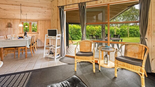 A wooden cabin with a dining area, a computer desk, wicker chairs, and large windows offering a view of the garden. - "Åsa" - 500m to the fjord by Interhome (Tarm)