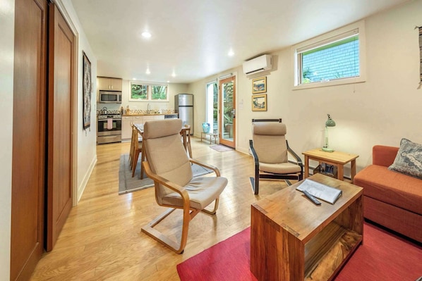Un espacio habitable amplio con una cocina al fondo, piso de madera y un tapete rojo.