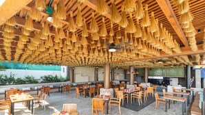 Un espace de restauration en plein air avec des tables et des chaises en bois, un coin salon couvert agrémenté de guirlandes décoratives, et une vue sur la plage.