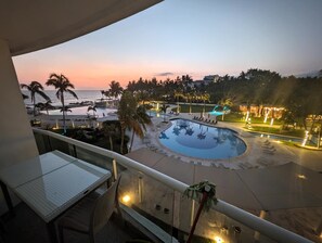 Zona de piscina con sillones reclinables y palmeras, vista desde un balcón.