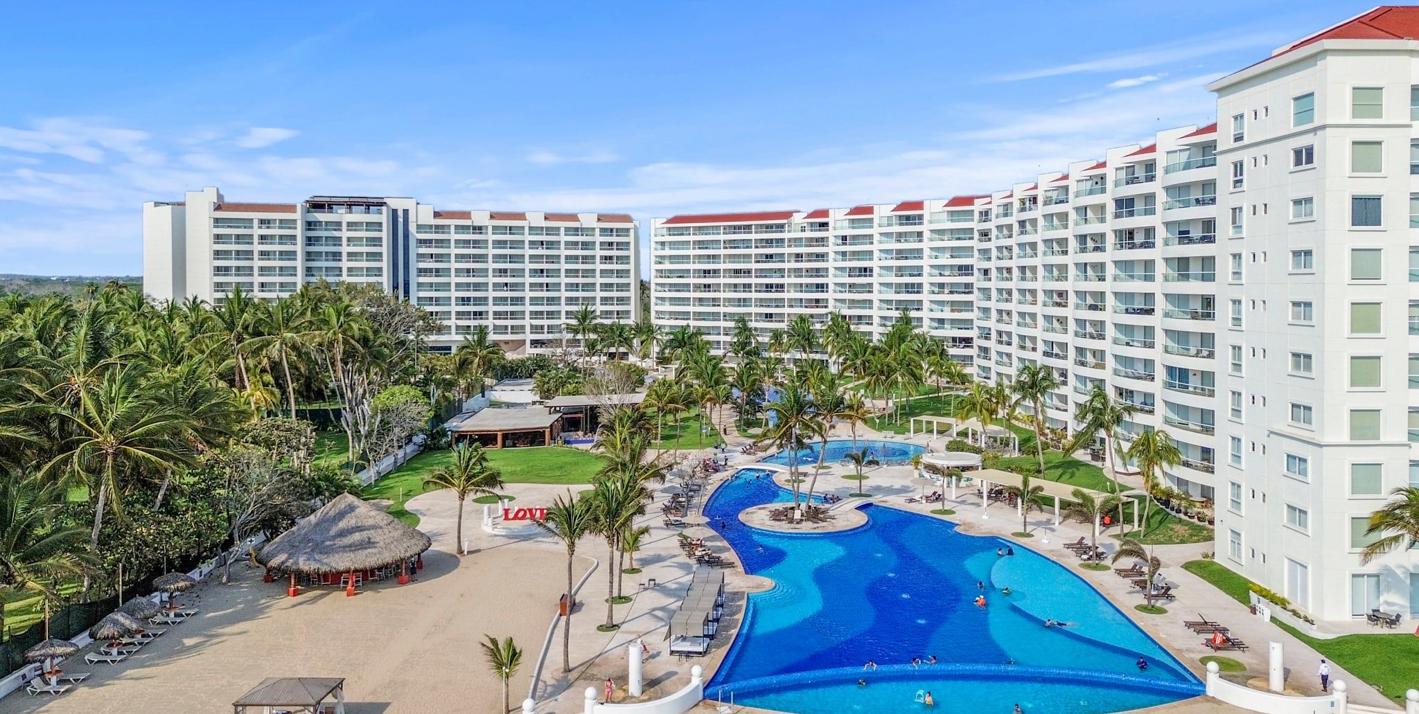 A resort with a large pool, palm trees, and a hotel building with multiple balconies.