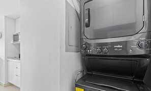 Une cuisine moderne équipée d’un lave-linge et d’un sèche-linge intégrés, de meubles blancs et d’un four à micro-ondes.