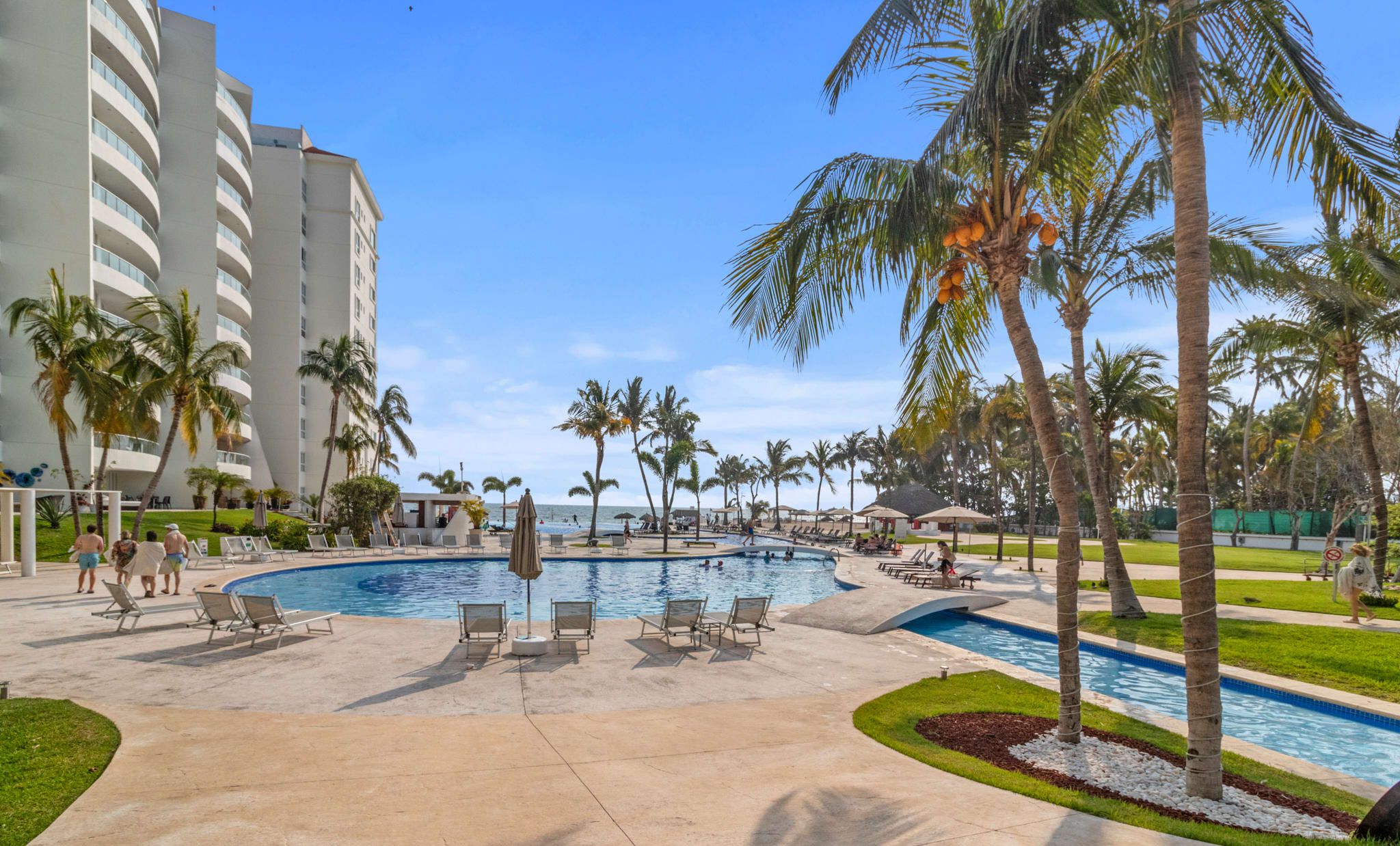 A pool area with lounge chairs, palm trees, and a building in the background.
