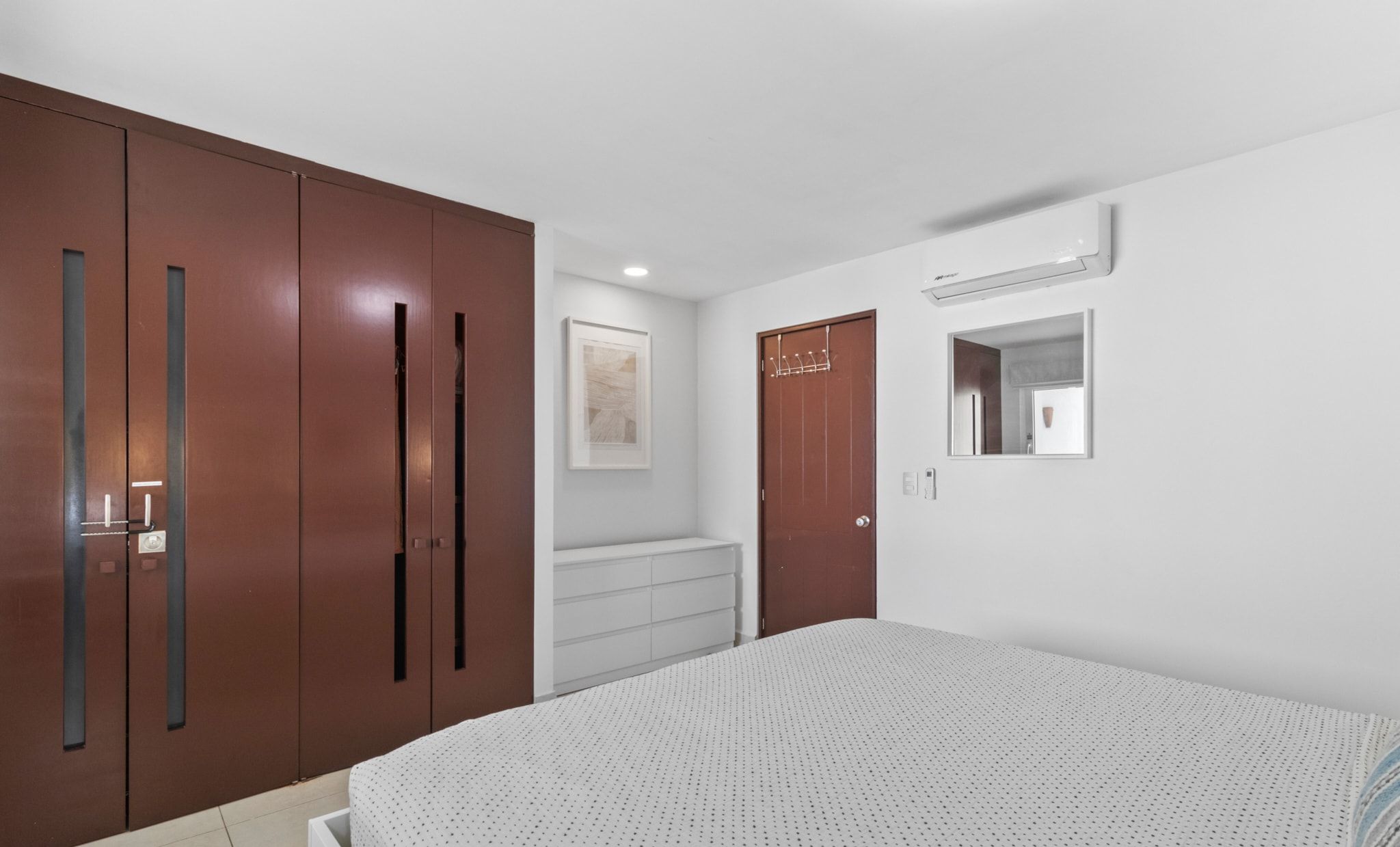 A bedroom with a large bed, wooden wardrobe, and a small dresser.