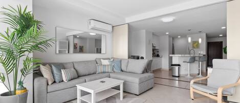 Ein modernes Wohnzimmer mit einem grauen Sofa, einem weißen Couchtisch und einer großen Topfpflanze.