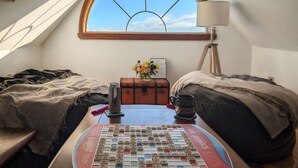 Une chambre confortable située dans les combles, avec un puits de lumière, un jeu de Scrabble, une vieille malle et une lampe.