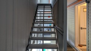 Un escalier étroit avec des rampes en métal, menant à une porte à l’extérieur blanche.