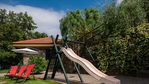 Une aire de jeux avec un toboggan, des balançoires et des chaises rouges.