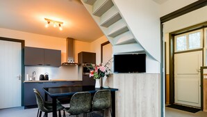 A modern kitchen with dark cabinets, a central island, and a dining area with a table and chairs. - Cosy house in wooded surroundings (Erp)