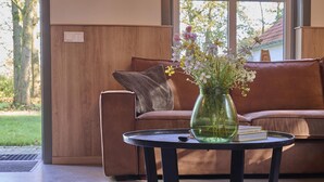 A modern living room with a brown leather sofa, a round black coffee table, and a green vase with flowers. - Cosy house in wooded surroundings (Erp)
