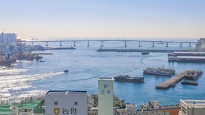 Un paysage urbain côtier avec un grand pont enjambant une étendue d’eau, plusieurs bateaux amarrés dans une marina et un bâtiment imposant avec une enseigne visible au premier plan.