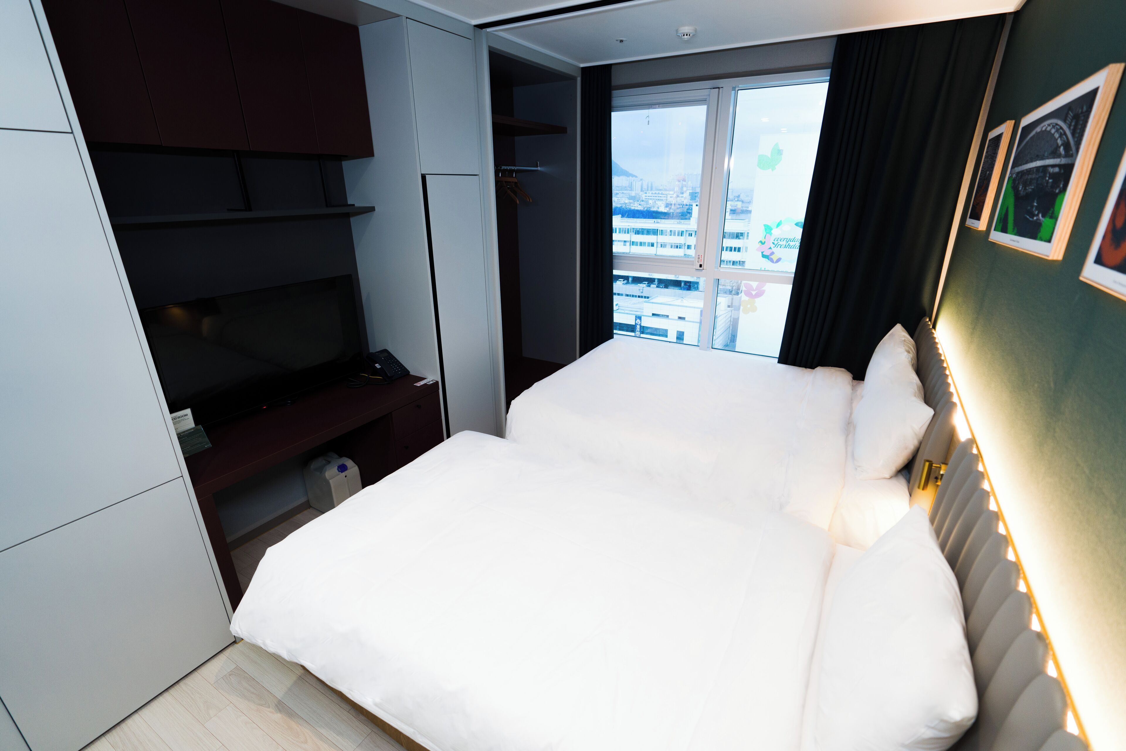Une chambre d’hôtel moderne, dotée d’un grand lit, d’une armoire et offrant une vue sur la ville grâce à une grande fenêtre.
