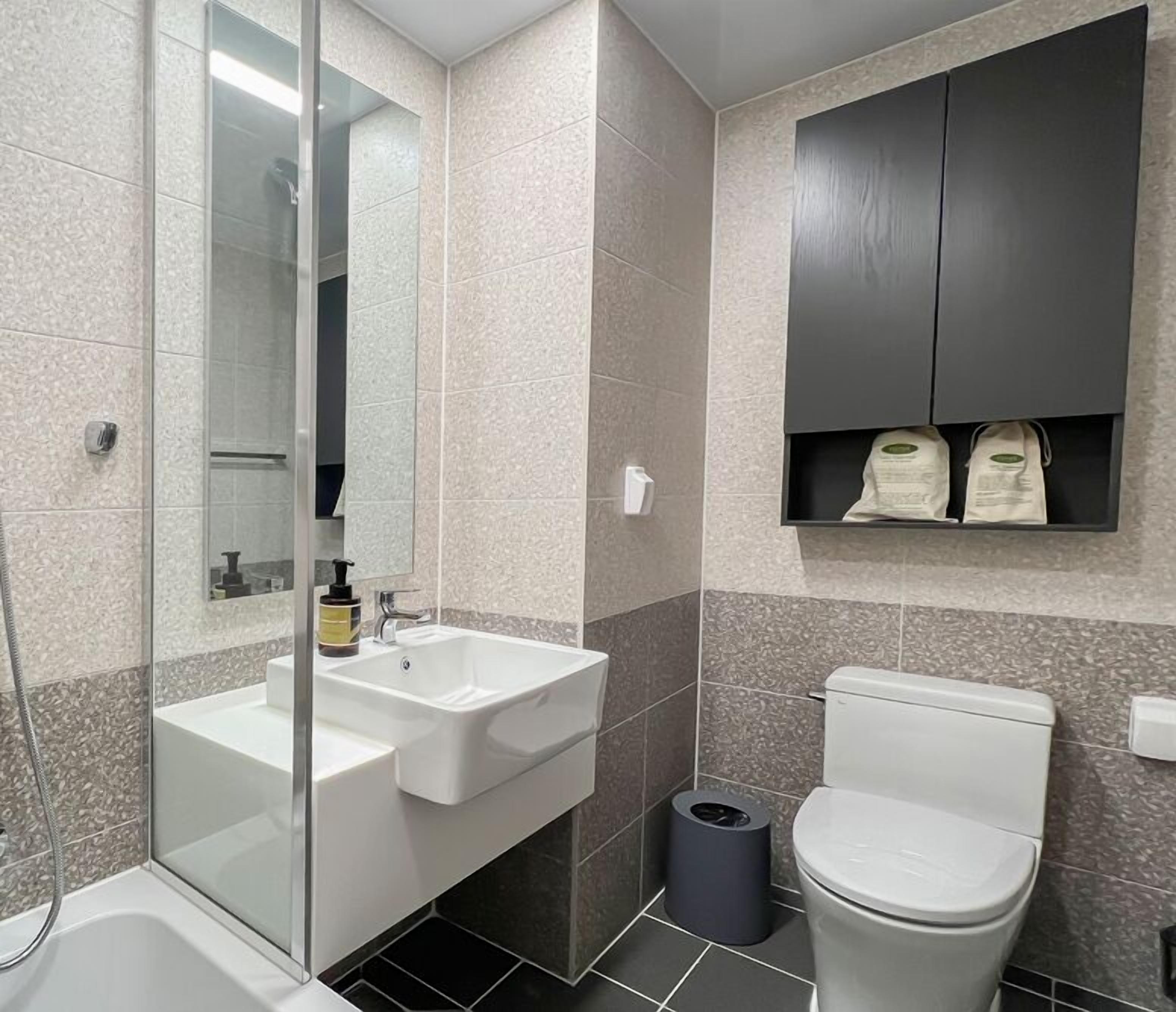 A modern bathroom with a glass-enclosed shower, a white sink with a mirror, and a toilet with a dark cabinet above it.