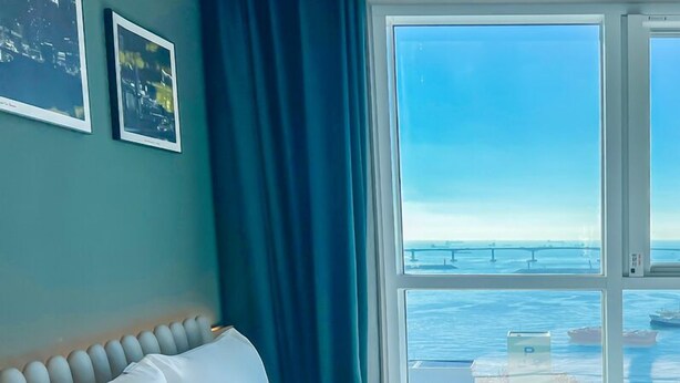 Une chambre d’hôtel avec un lit, une grande fenêtre donnant sur la mer et deux tableaux encadrés accrochés au mur.