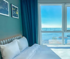 Habitación de hotel con cama, un ventanal con vistas al mar y dos cuadros en la pared.