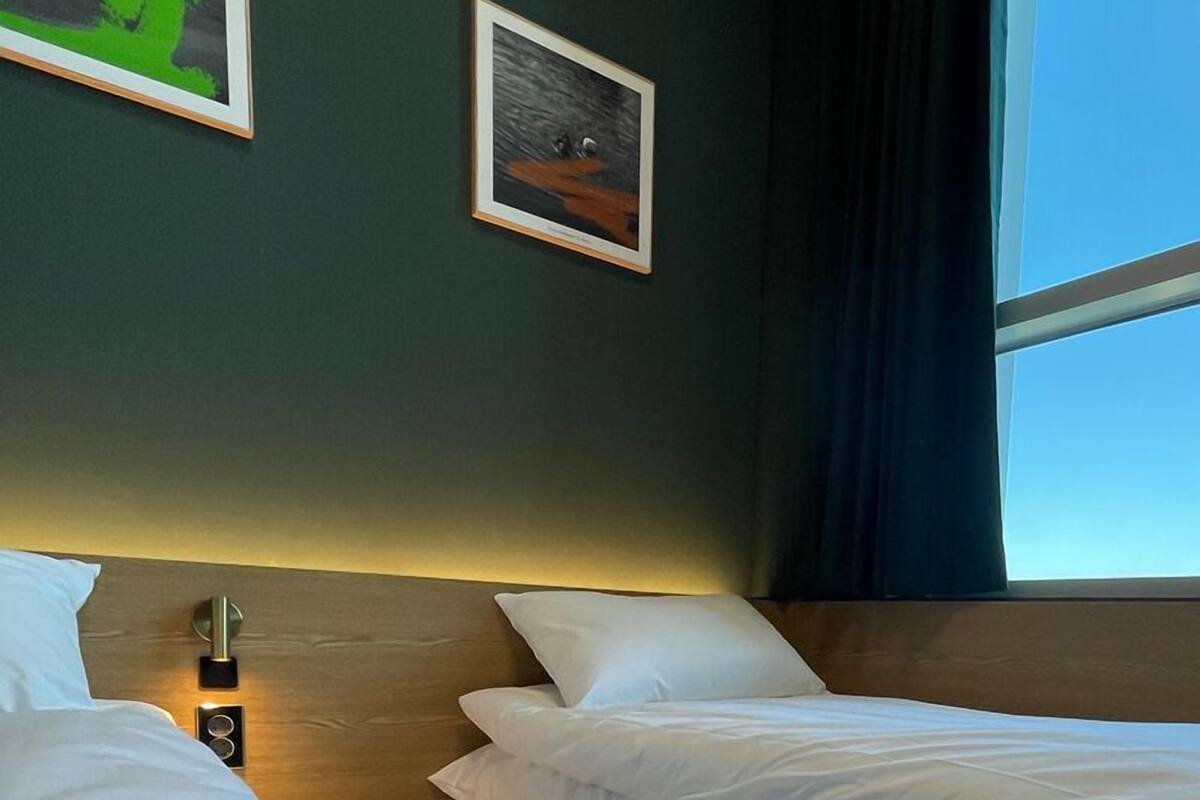 Una habitación de hotel con dos camas, una mesita de noche y una ventana con cortinas.