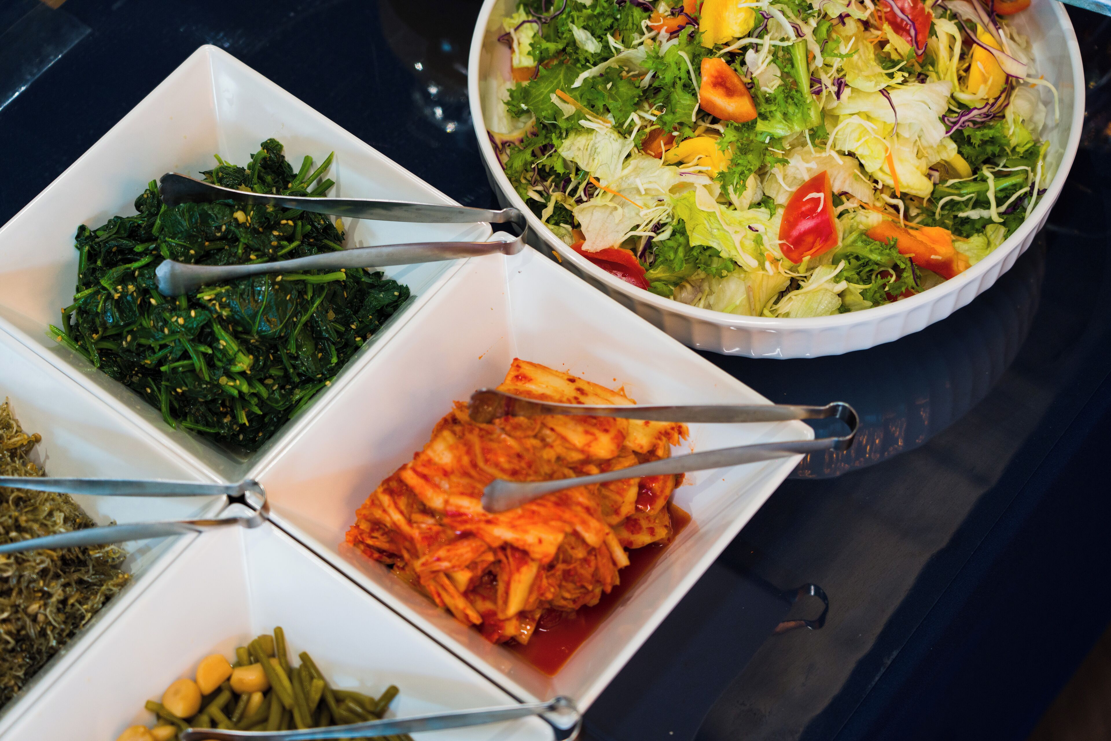 Een buffet met diverse gerechten, waaronder salade, kimchi en andere gemengde groenten.