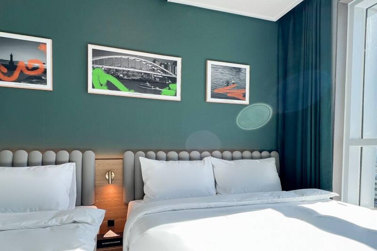 Una habitación de hotel con dos camas, una mesita de noche y una pared con tres cuadros enmarcados.