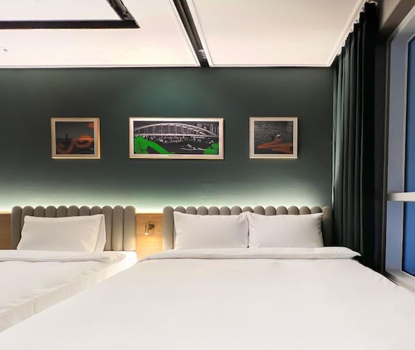 Habitación de hotel con dos camas, un cabecero y tres cuadros en la pared.