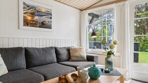 A cozy living room with a grey sofa, a wooden coffee table with pastries and mugs, a teal teapot, and a framed landscape photo on the wall. - "Horsten" - 270m from the sea by Interhome (Nexø)